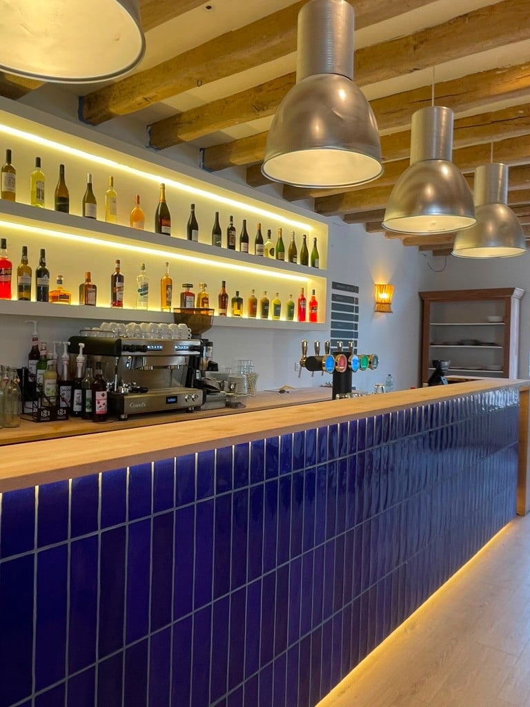 Le bar en bois et carrelage bleu, machine à espresso et tireuses à bière.