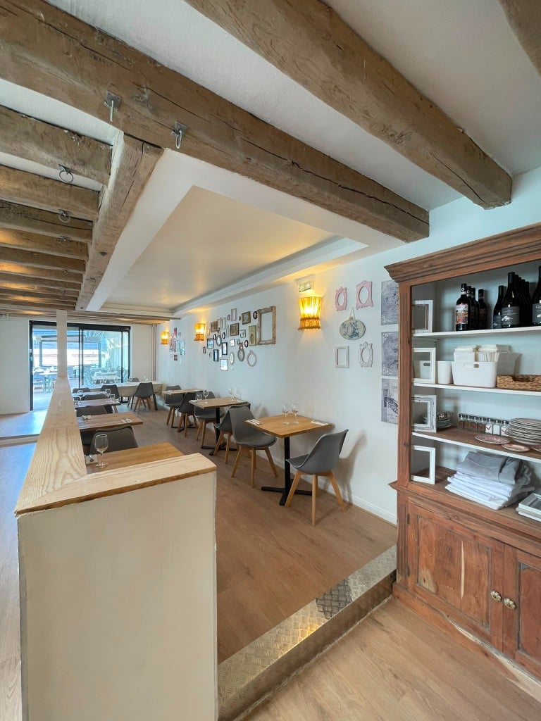 Coin de la salle avec cadres au mur, vaisselier en bois et verres sur les tables.