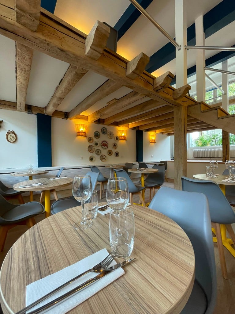 La salle avec tables rondes, poutres apparentes et assiettes décoratives au mur.