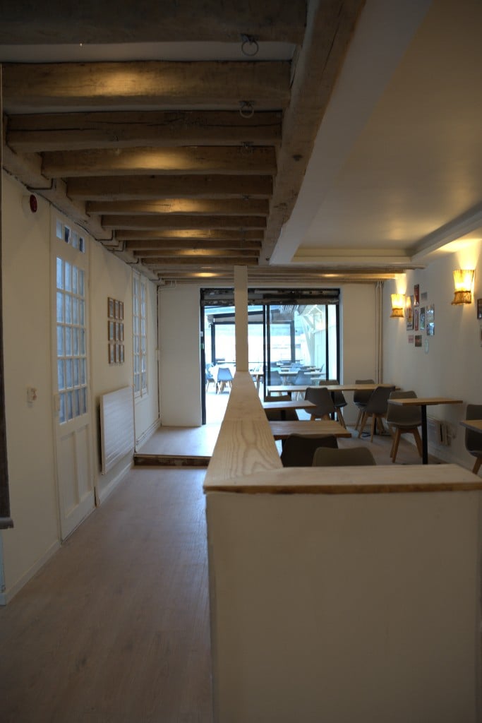 Vue de la salle vers la terrasse, poutres en bois et lumière naturelle.