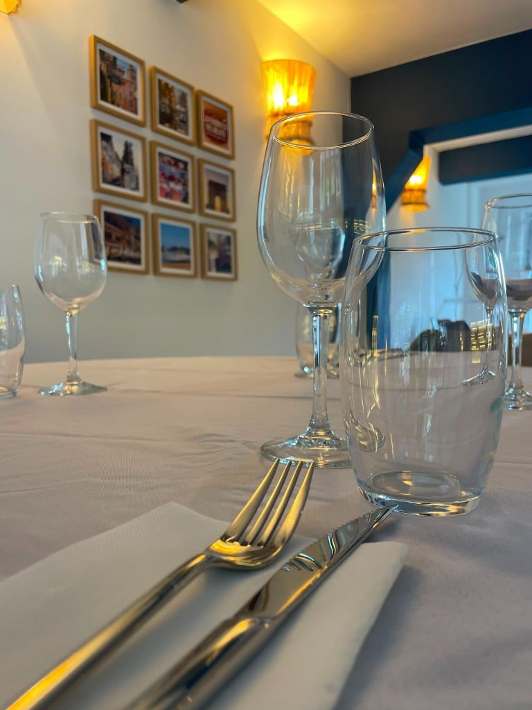 Table dressée avec verres et cadres photos au mur, lumière chaude.
