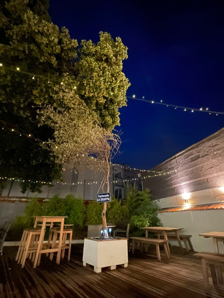 Terrasse extérieure éclairée le soir, guirlandes lumineuses et tables en bois.