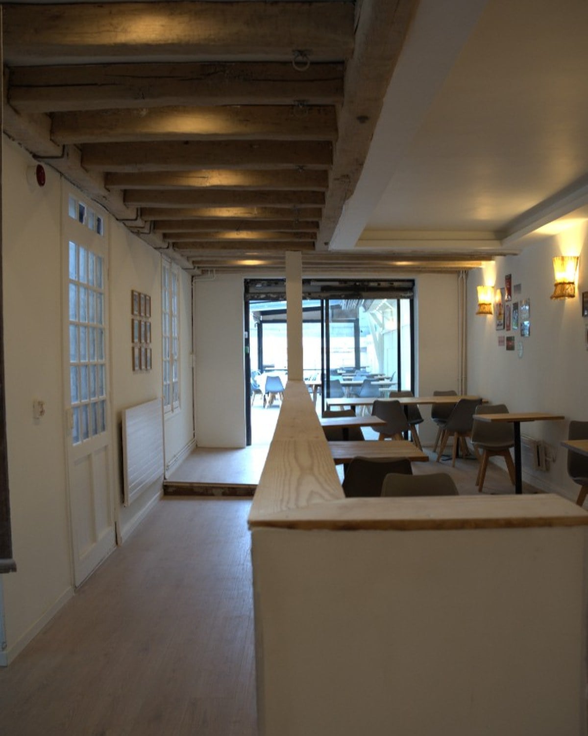 La salle de Jean & Gino à Reims, poutres apparentes, tables dressées et lumière naturelle en fond.